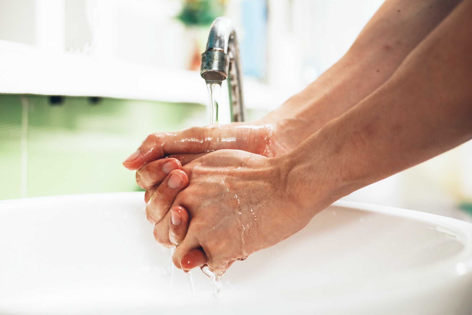 Close-up of human hands washing away germs and bacteria under the sanitary crane.